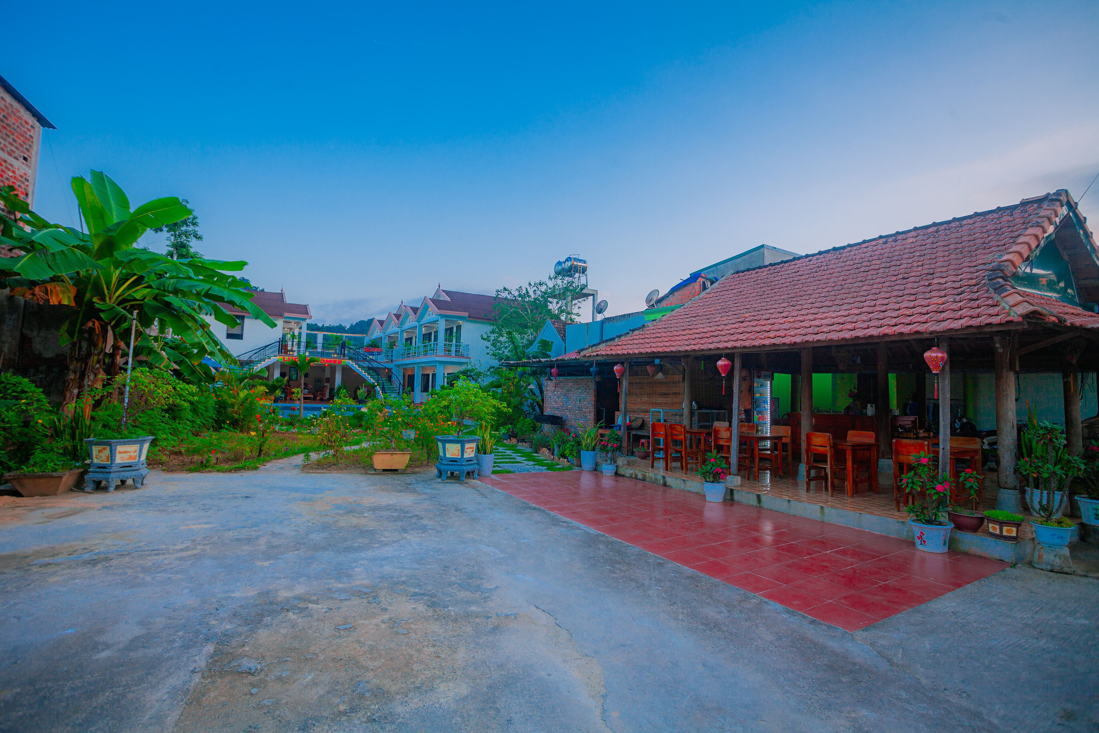 A courtyard with a red-tiled floor, potted plants, and a building with a red-tiled roof.