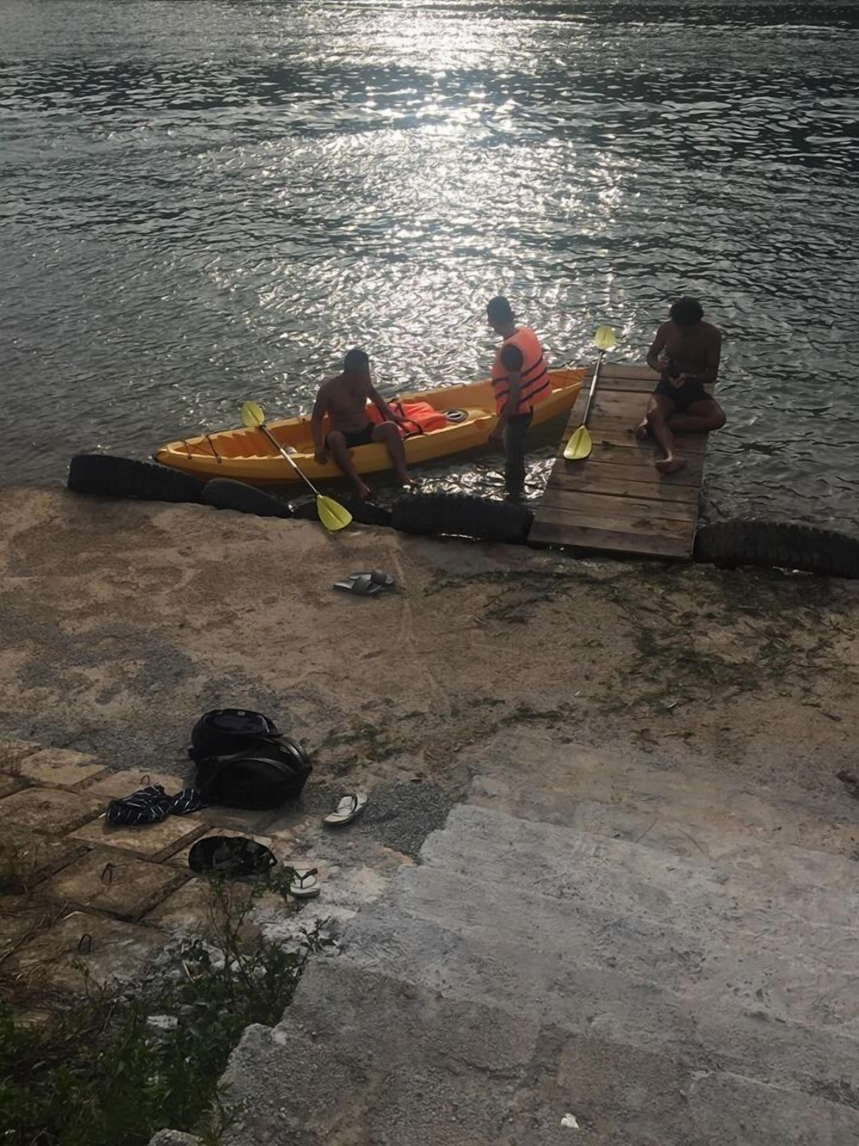 Un quai où se trouvent trois personnes : une est dans un kayak et les deux autres sont sur le quai, à proximité d’une étendue d’eau calme.