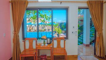 Una habitación con una mesa de madera y dos sillas, una ventana con cortinas y vistas a una zona de piscina al aire libre.