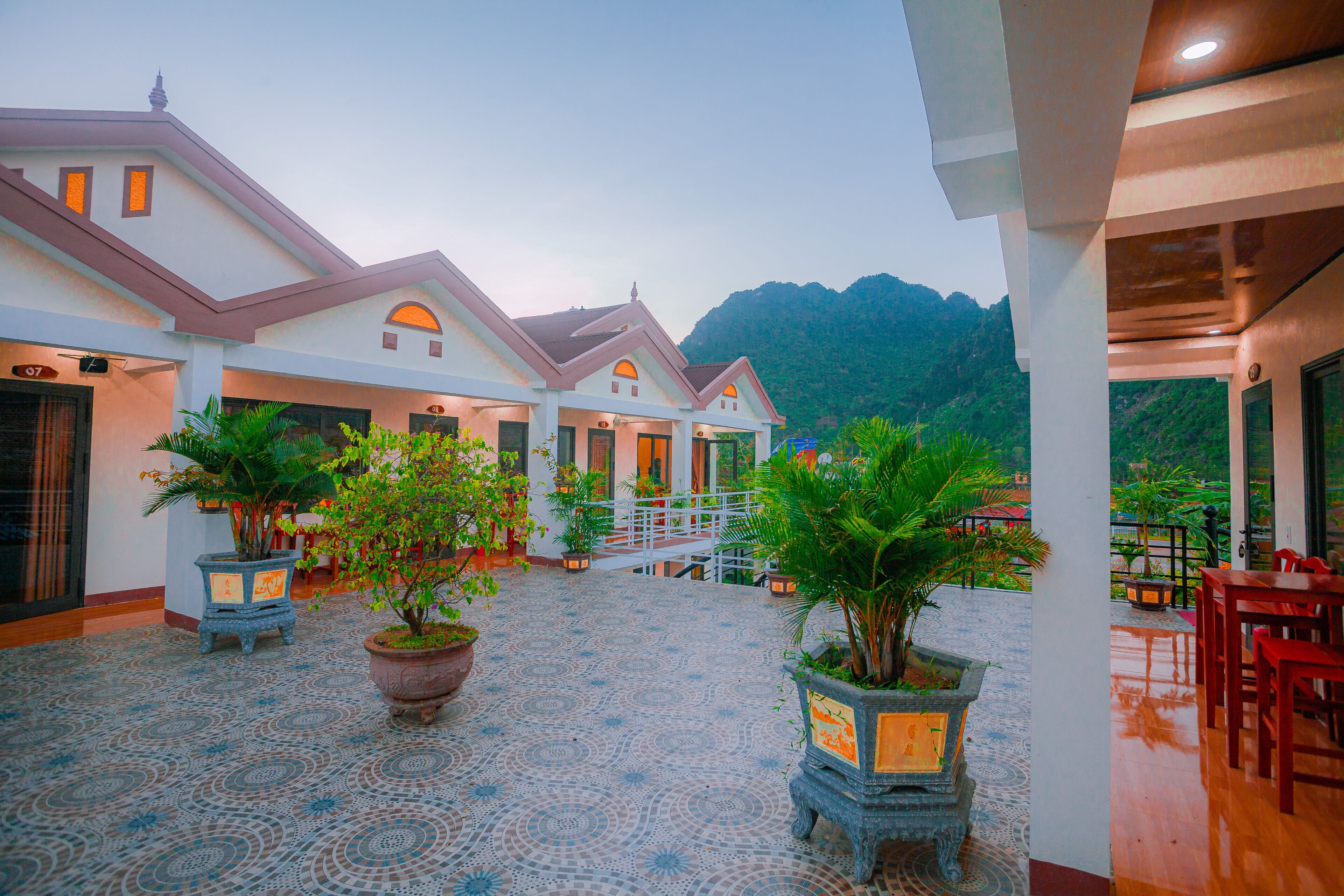 A hotel courtyard with potted plants, a tiled floor, and a view of mountains.