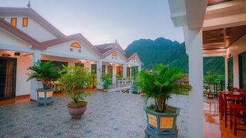 A hotel courtyard with potted plants, a tiled floor, and a view of mountains.