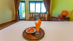 A hotel room with a bed, a dining table with a fruit plate and a glass of orange juice, and a view of the outdoors through the window. - Lucky Homes (Phong Nha)