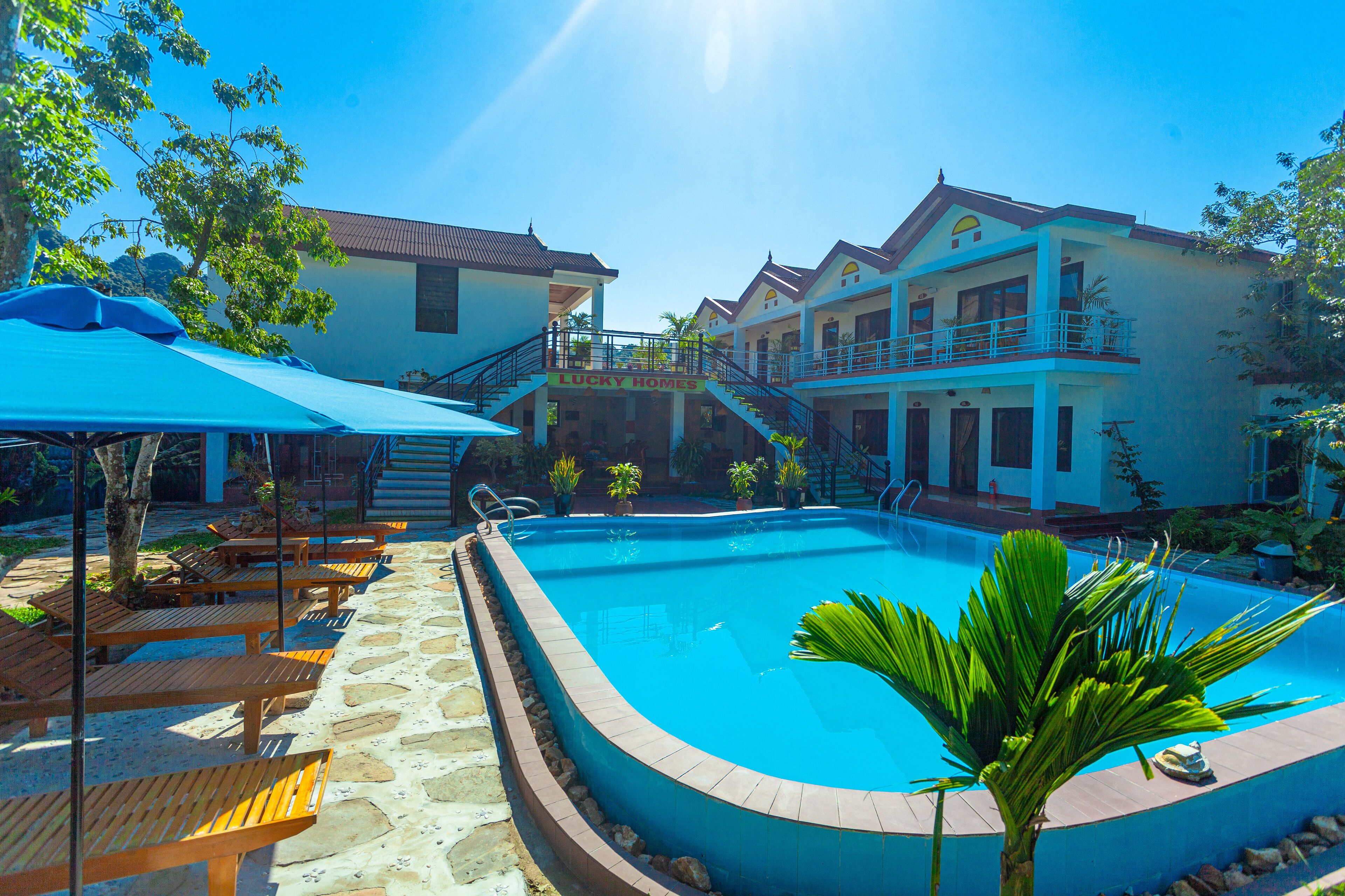 A pool area with a clear blue pool, wooden lounge chairs, and a staircase leading to a building labeled "Lucky Homes".