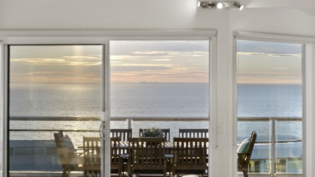 A room with a view of the sea, a balcony with wooden chairs, and a table.