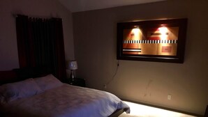 A bedroom with a bed, a nightstand, a lamp, and a wall-mounted light fixture. - Westside El Paso Beautiful Big House lots of Perks contemporary nice Backyard (El Paso)