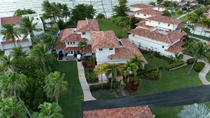 Un quartier résidentiel où les maisons se distinguent par leurs toits recouverts de tuiles rouges, entouré d’une végétation luxuriante et de palmiers, avec une vue sur l’océan en arrière-plan.