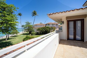 A balcony with a view of the ocean and palm trees, a tiled floor, and a door with a window.