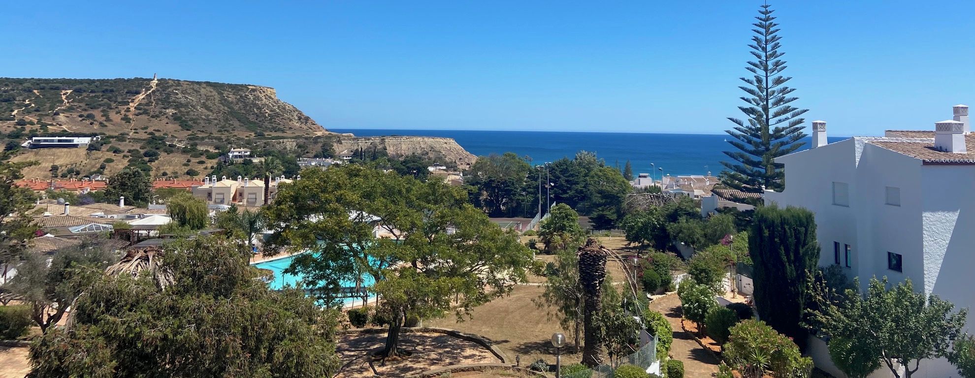 A residential area with a pool, trees, and a view of the sea.
