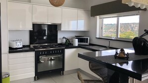 Una cocina moderna con armarios blancos, una estufa negra, un microondas y un amplio ventanal con vistas a las colinas.