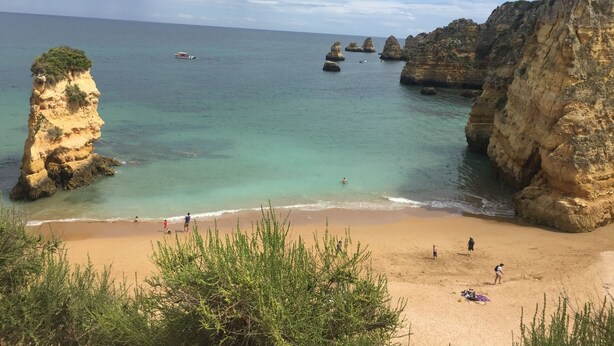Una playa costera con aguas turquesas cristalinas, acantilados rocosos y una orilla arenosa.