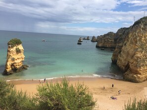 A coastal beach with clear turquoise waters, rocky cliffs, and a sandy shore.