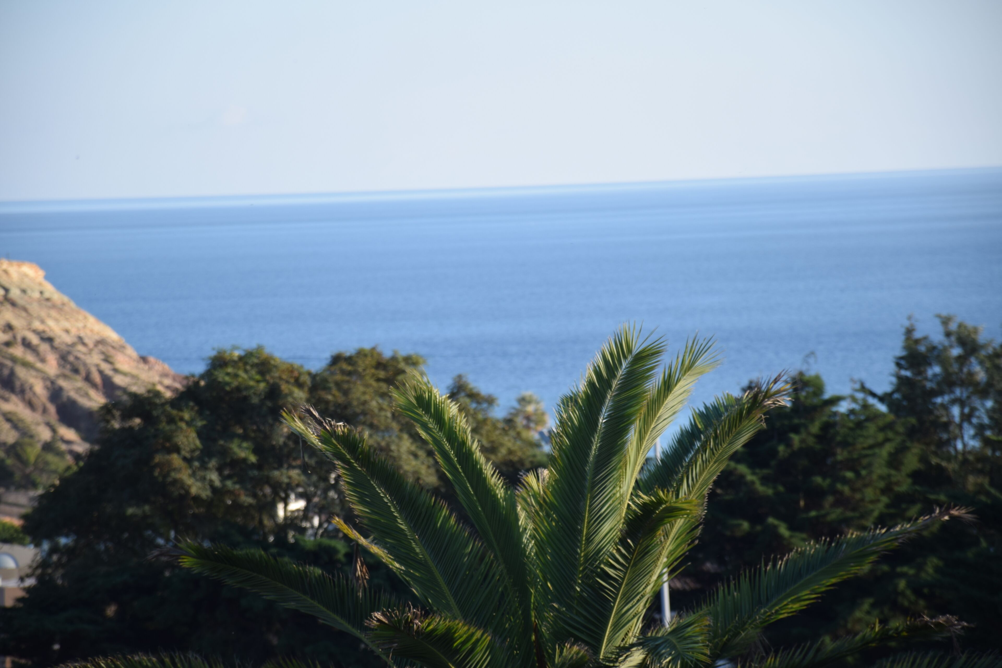 A coastal view with a clear sky, a body of water, and a mountain in the background.