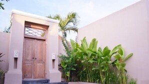 Une entrée d’immeuble avec une porte en bois, des marches menant à cette porte et un mur orné de plantes vertes.