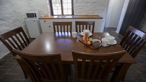 A dining area with a wooden table, six chairs, a microwave, and a sink. - Paxton Square (Burra)