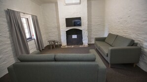 A room with a stone fireplace, a flat-screen TV mounted above it, and a grey sofa. - Paxton Square (Burra)