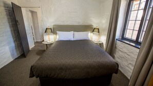 A bedroom with a large bed, two bedside lamps, a window with curtains, and a door leading to another room. - Paxton Square (Burra)