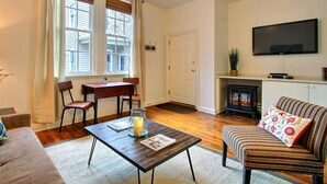 A cozy living room with a fireplace, a flat-screen TV, a dining table with chairs, and a sofa. - Fountain View Cottage, Beautiful Savannah Home (Savannah)
