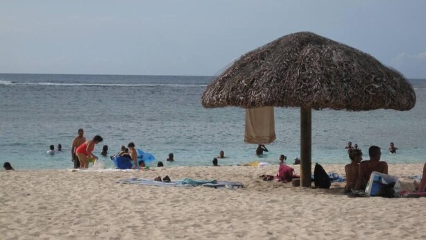 Een strand met mensen die zwemmen en ontspannen onder een rieten parasol.