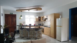 Een moderne keuken met een centraal eiland, barkrukken, een koelkast en houten kastjes.