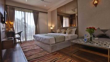 Ein modernes Hotelzimmer mit einem großen Bett, einer Sitzecke mit einer Couch, einem Couchtisch und Blick ins Freie durch das Fenster.