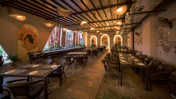 A restaurant with long communal tables, individual chairs, and a high ceiling with exposed beams. - Hotel President Cottage Resort (Jalgaon)