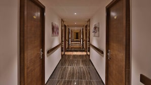 A hotel hallway with wooden doors, marble flooring, and artwork on the walls. - Hotel President Cottage Resort (Jalgaon)