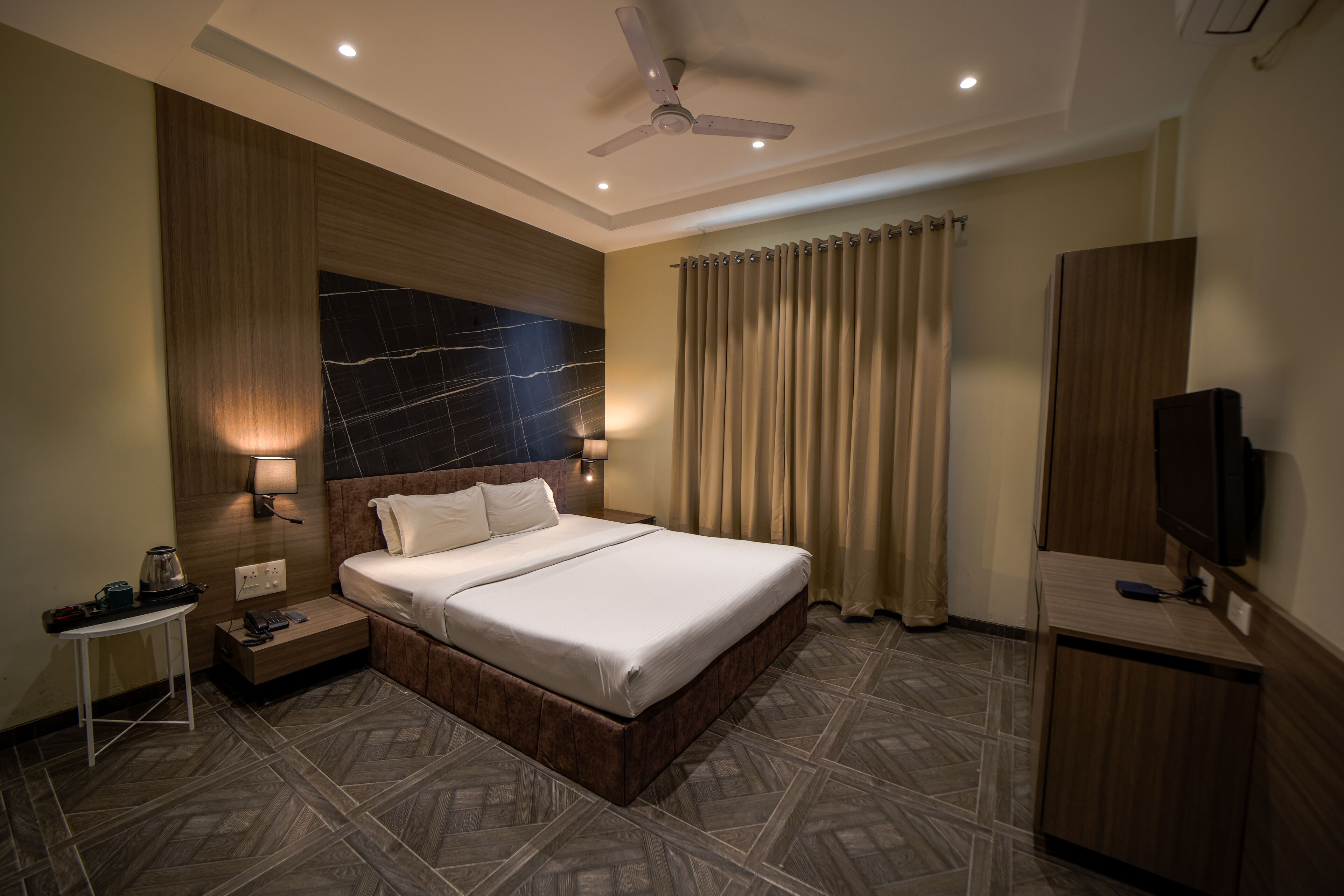Quarto de hotel com uma cama grande, uma escrivaninha com luminária, televisão e ventoinha de teto.