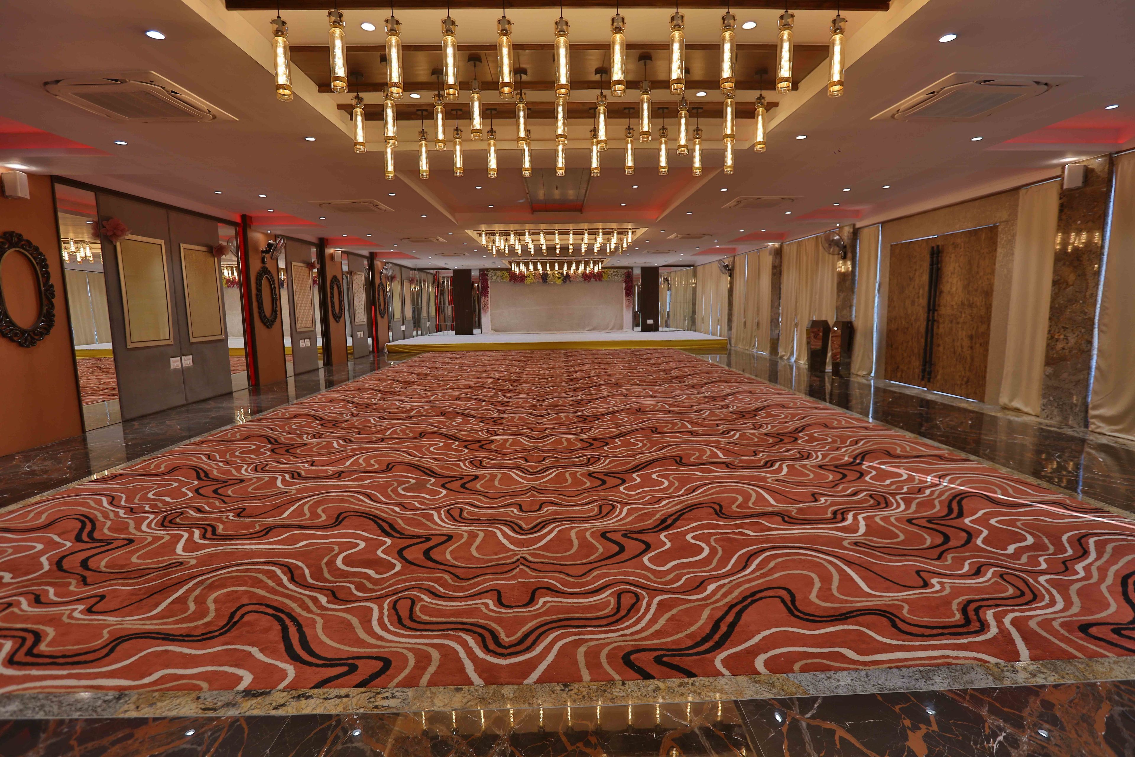 A spacious corridor with a patterned carpet, reflective floor, and a series of doors on one side.