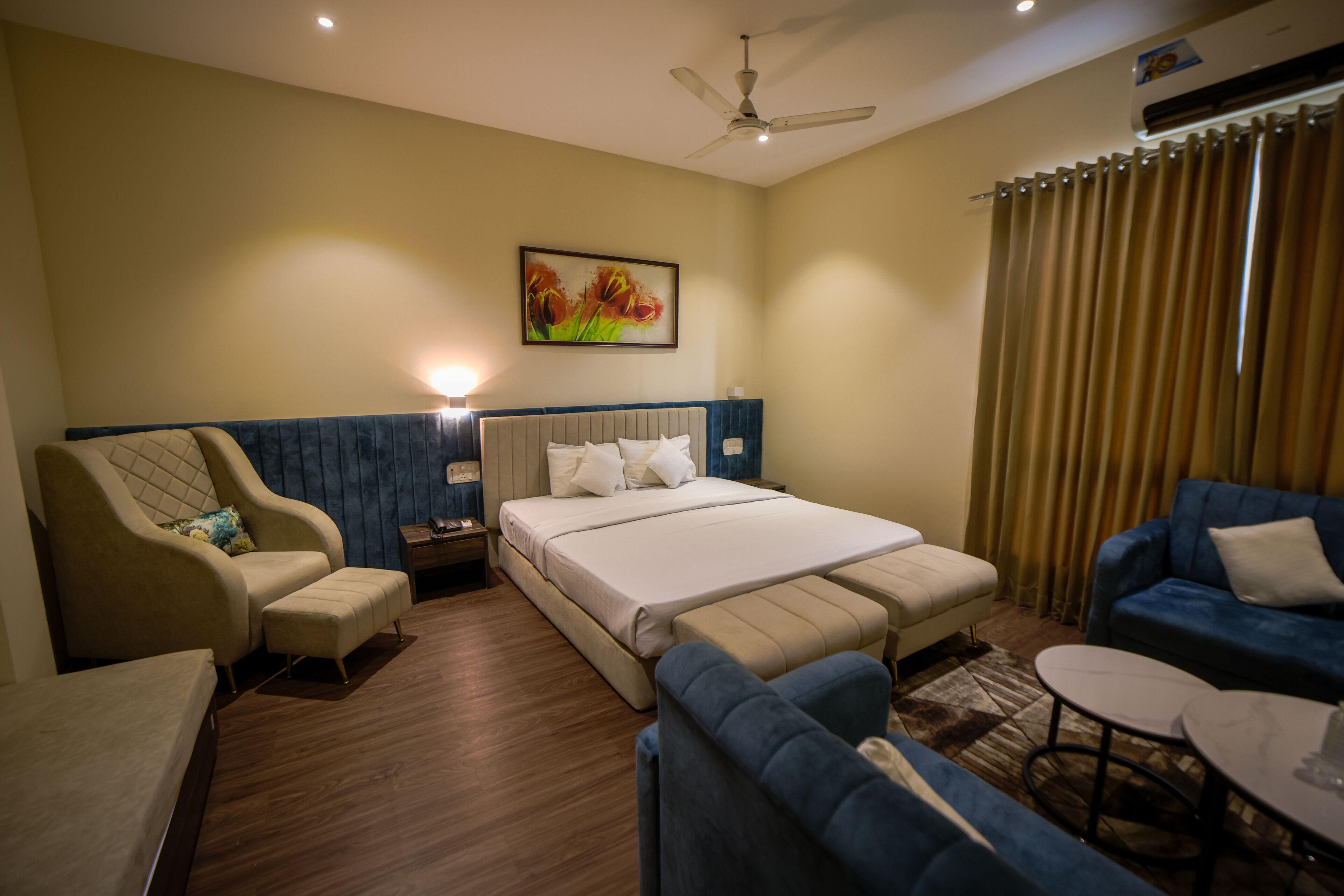 A hotel room with a bed, a sofa, a chair, a small table, and a ceiling fan.