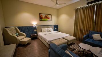 A hotel room with a bed, a sofa, a chair, a small table, and a ceiling fan.