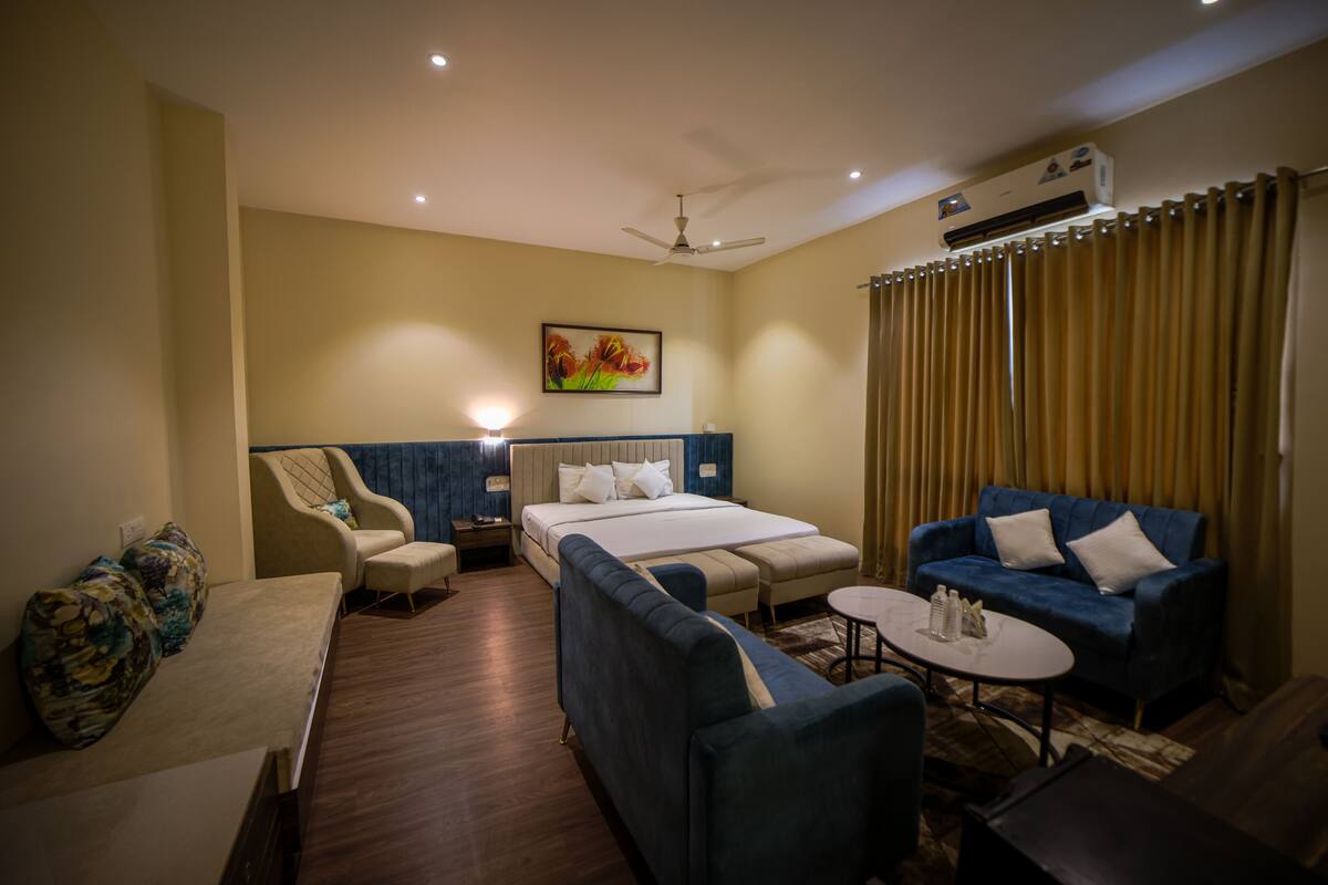 A hotel room with a bed, a sofa, a chair, a small table, and a ceiling fan.
