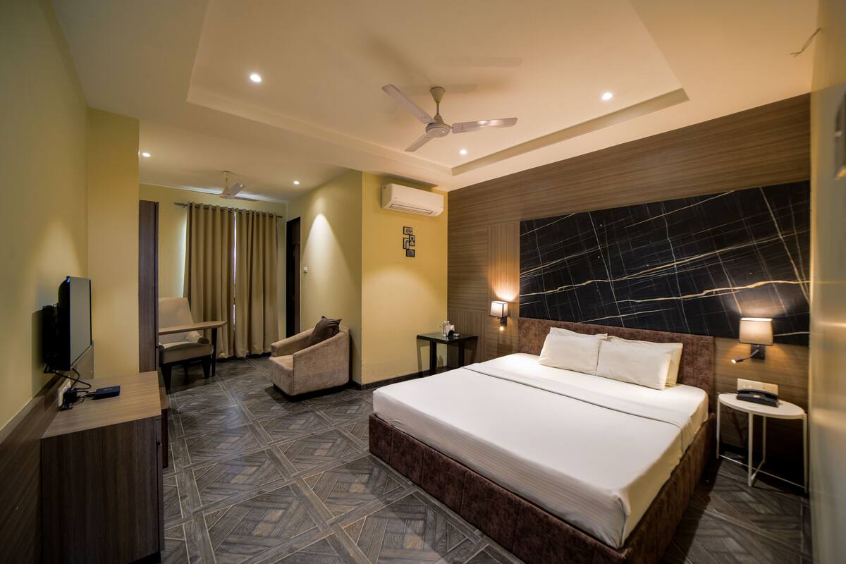 A hotel room with a large bed, a desk, a chair, a TV, and a ceiling fan.