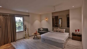 A modern hotel room with a large bed, a sofa, a small round table, and a nightstand. - Hotel President Cottage Resort (Jalgaon)