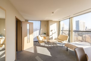 Quarto de hotel moderno com uma grande janela, uma escrivaninha com cadeira e um sofá.