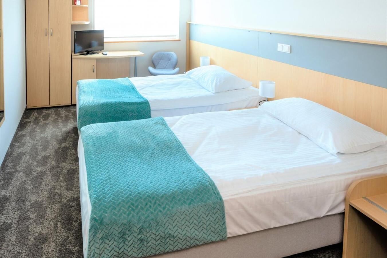 A hotel room with two beds, a desk with a computer, a chair, and a TV.