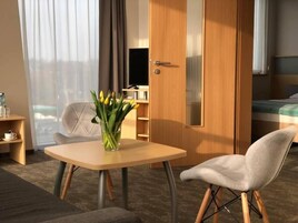 Quarto de hotel com cama, escrivaninha, cadeira, televisão e janela com cortinas.