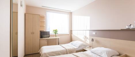 A hotel room with two beds, a desk with a TV, a window, and a wardrobe.