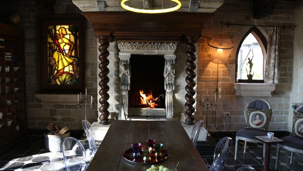 A dining area with a fireplace, stained glass window, and a table set with a fruit bowl and glasses.