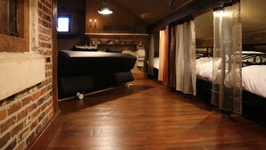 A narrow, wooden-floored room with a bed on wheels, a brick wall, and a window with natural light.