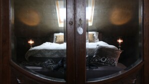 A bedroom with a large mirror, two bedside tables with candles, a bed with patterned bedding, and a window with natural light.