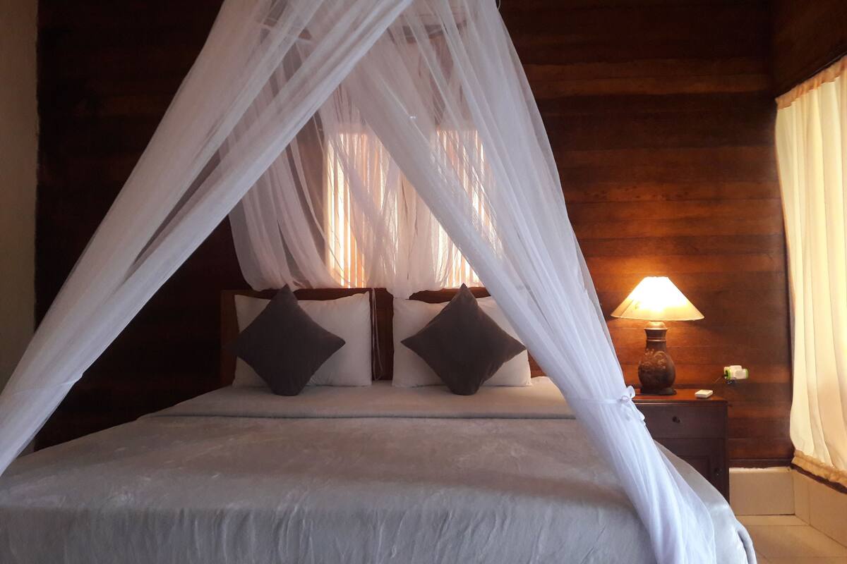 A bed with a canopy, two pillows, a nightstand with a lamp, and wooden walls.