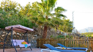 Un patio con una silla mecedora, tumbonas y una palmera.