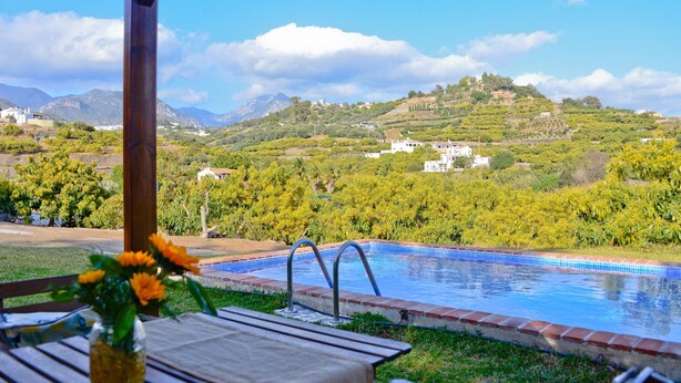 Una piscina con vistas a una ladera, una mesa de madera con un florero y una estructura de pérgola.