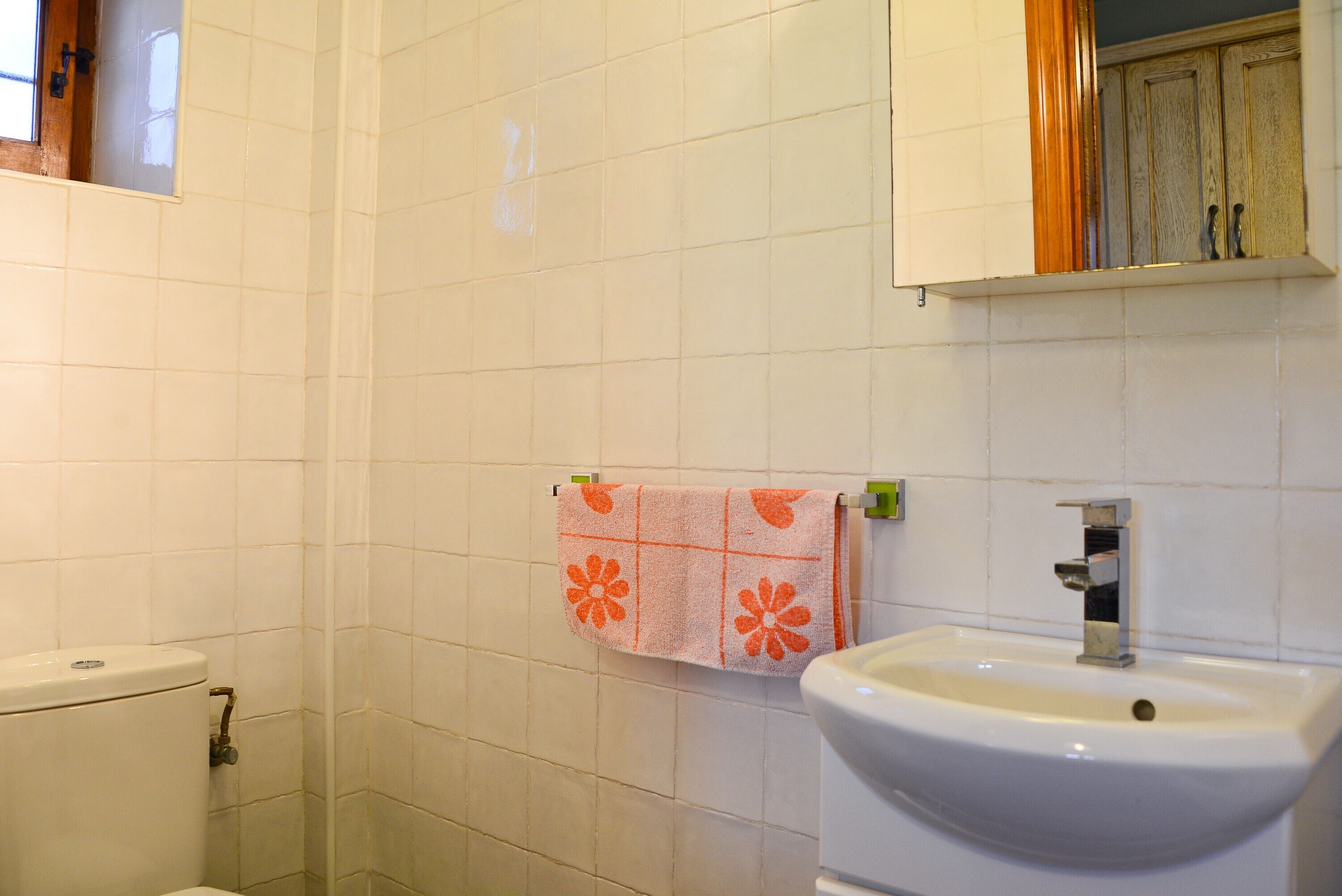 A bathroom with white tiles, a toilet, a sink, and a towel hanging on the wall.