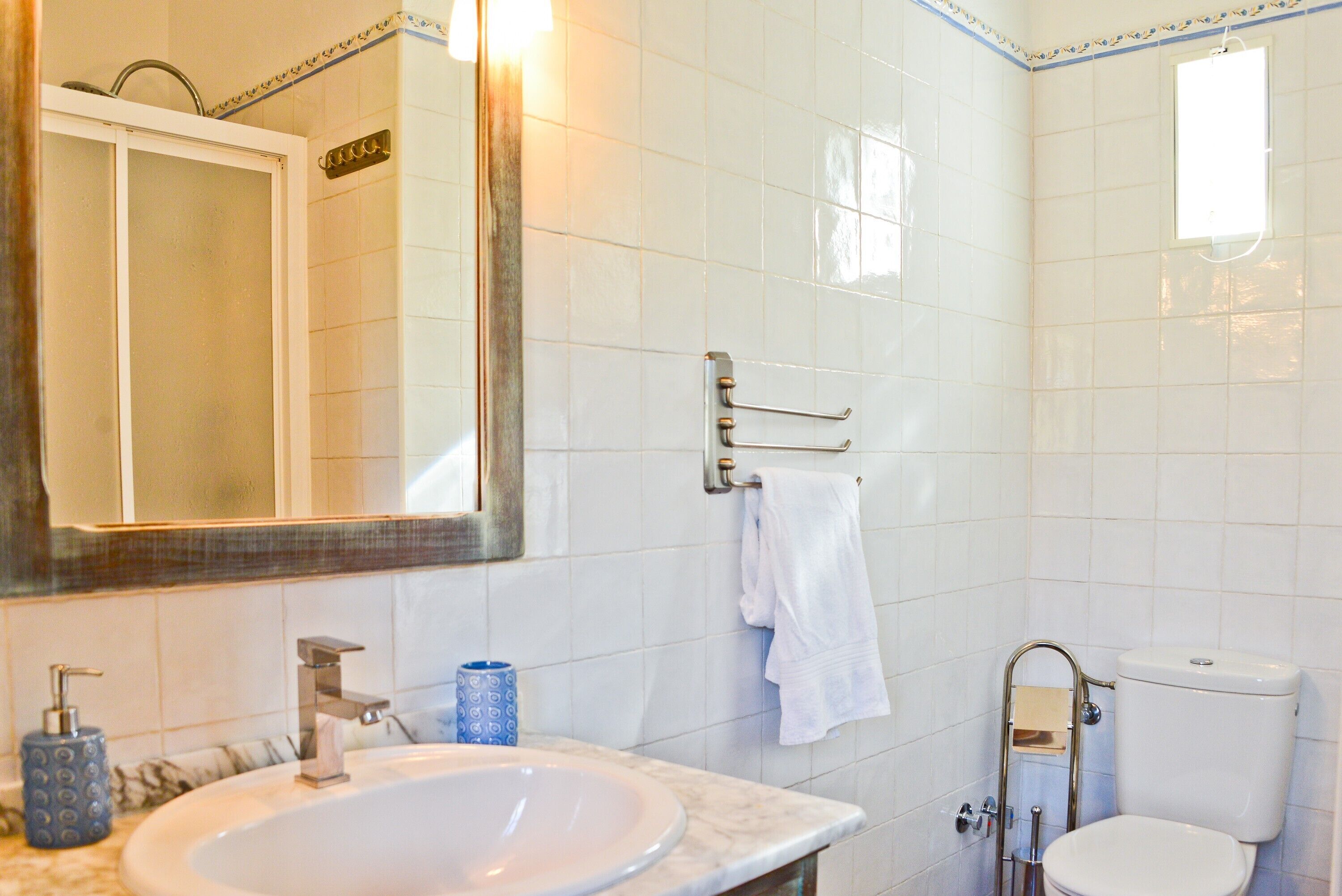 Un baño con lavamanos, espejo, toallero, inodoro y ventana.