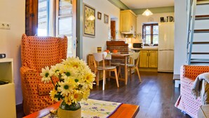 Una sala acogedora con un sillón estampado, una mesa de comedor con sillas y una cocina al fondo.