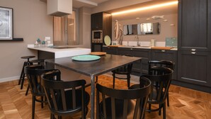 A modern kitchen with a central island, a dining area with chairs, and a large mirror above the sink. - Modern Apartment by the Lake (SALO)