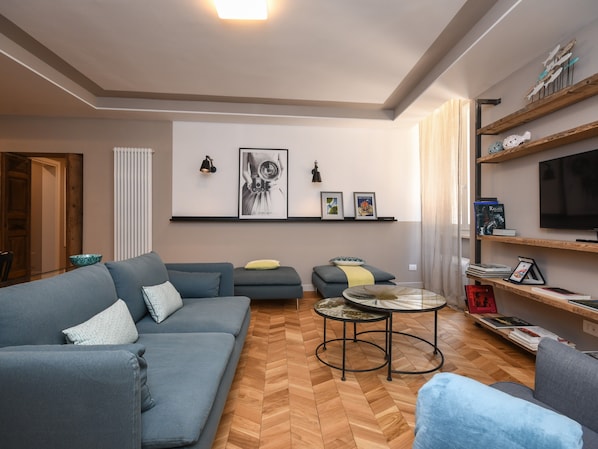 Un salon moderne avec un canapé, des fauteuils, une table basse et un téléviseur posé sur une étagère en bois.