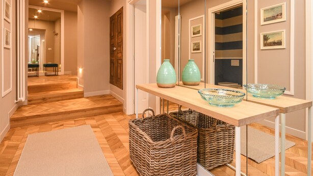 A hallway with wooden flooring, a mirror, a table with decorative vases, and wicker baskets. - Modern Apartment by the Lake (SALO)