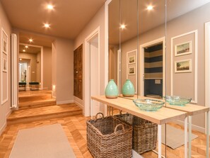 Un pasillo con piso de madera, un espejo, una mesa con jarrones decorativos y cestas de mimbre.